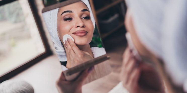 Woman looking at her even-looking skin in mirror while applying skincare
